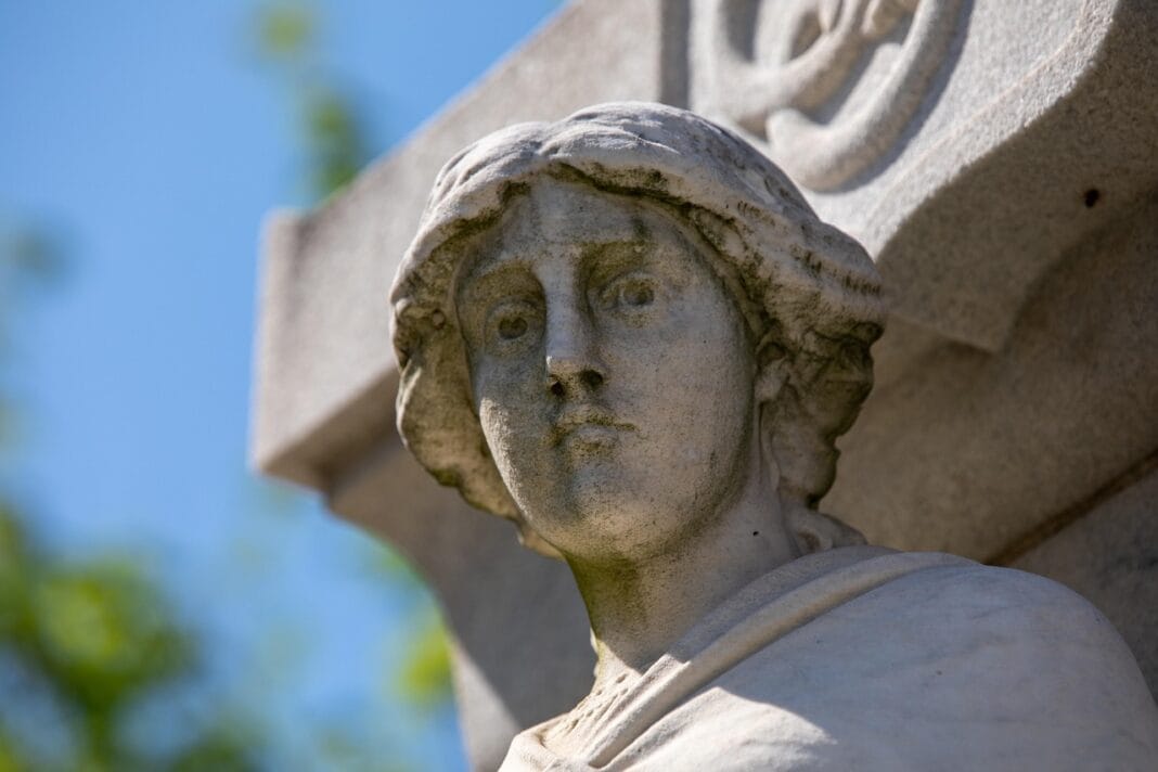 Escultura de pedra representando uma figura humana com expressão serena, fotografada sob luz natural contra um fundo azul. | Símbolo maçónico.