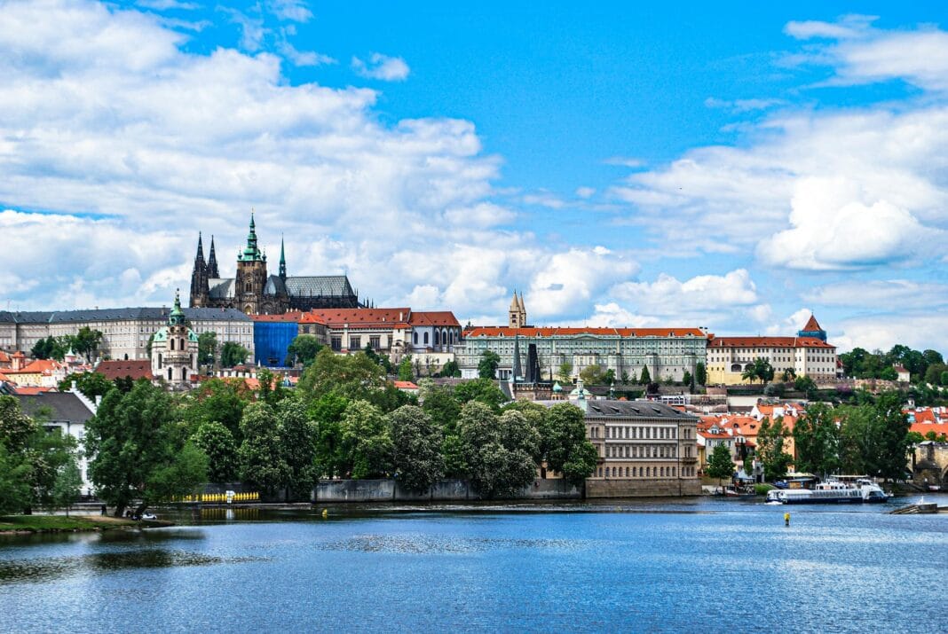 Vibrant view of Prague Castle and St. Vitus Cathedral across the Vltava River under a bright blue sky.