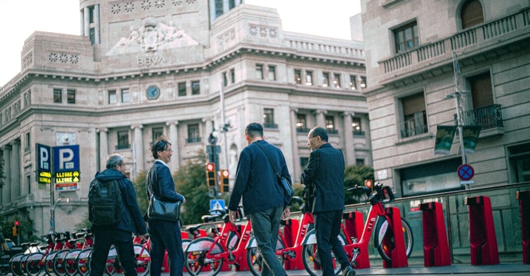Grupo de homens junto a bicicletas partilhadas numa praça urbana, em frente a um edifício histórico.