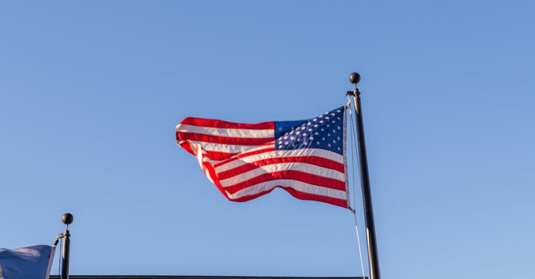 Bandeira dos Estados Unidos hasteada ao vento contra um céu limpo, simbolizando a tensão crescente no debate energético e político norte-americano.