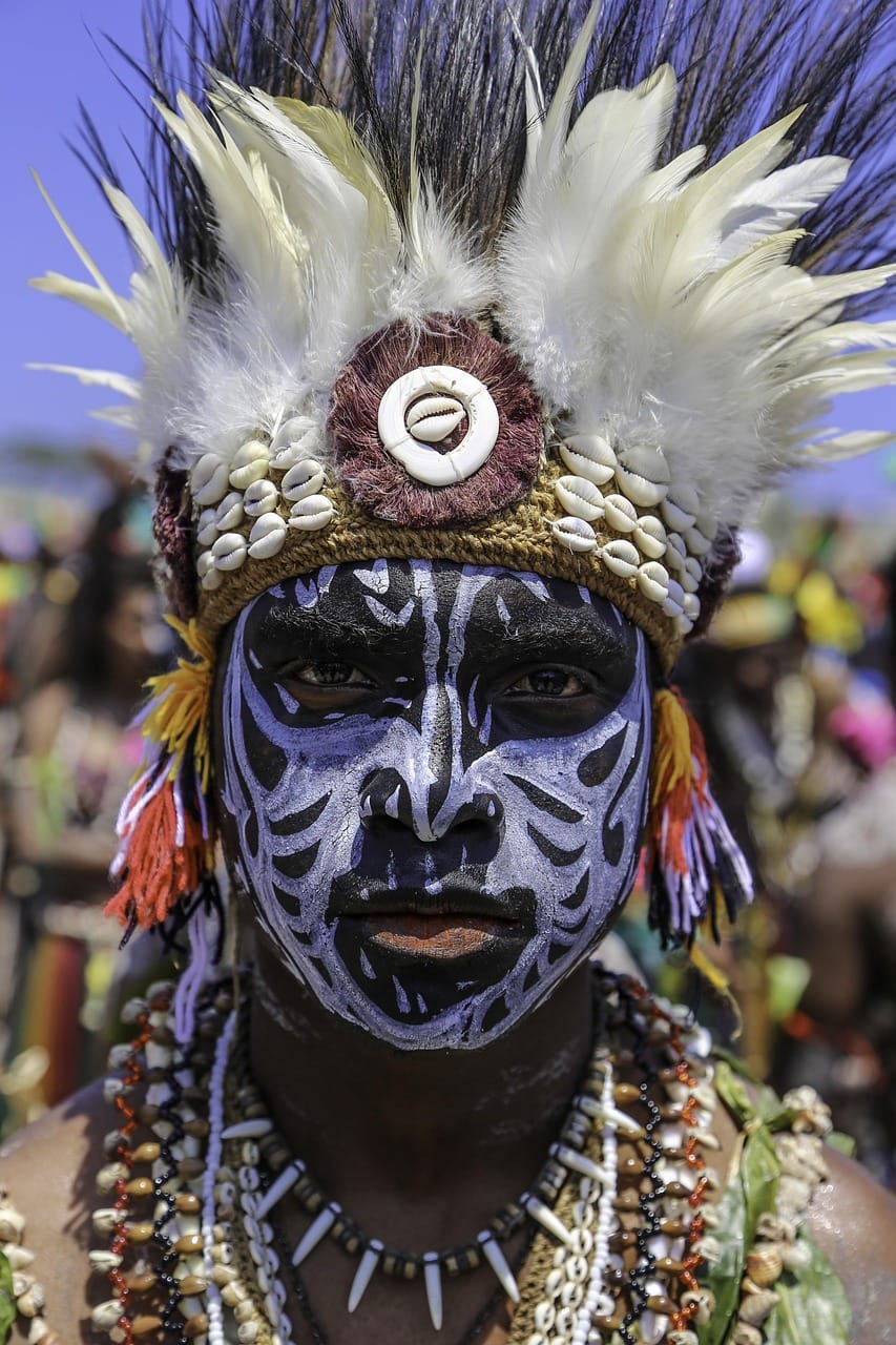Homem de Papua Ocidental com pintura facial tradicional e adereços cerimoniais, representando a diversidade cultural da região.