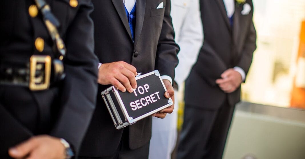 Homens em traje formal seguram uma mala com a inscrição “Top Secret”, evocando a natureza confidencial das reuniões entre os serviços de inteligência ocidentais.