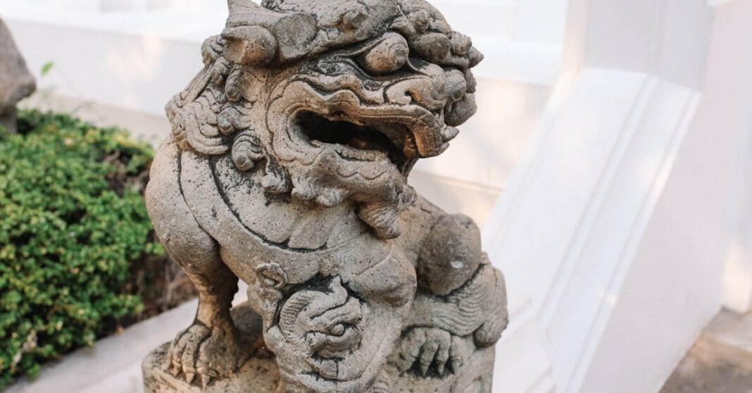 Escultura tradicional de um leão guardião em pedra num templo na Tailândia, fotografada em grande plano.