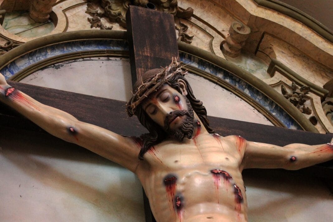 Crucifixo de Cristo numa igreja católica com decoração ornamentada dourada ao fundo
