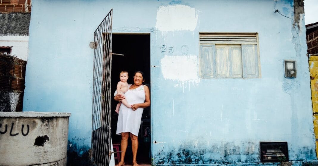 Mulher com um bebé ao colo à porta de uma casa de fachada azul.