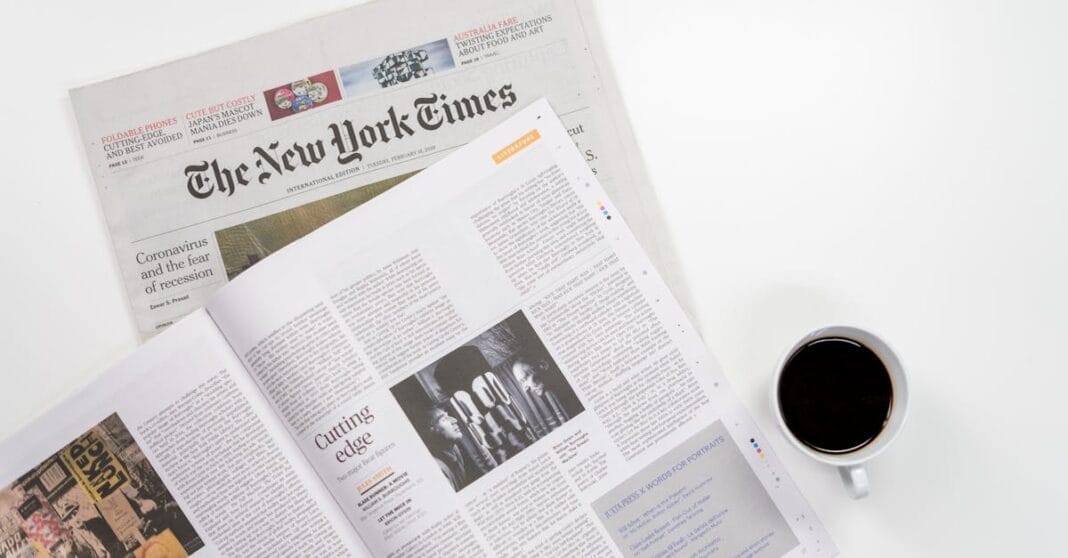 Uma mesa de trabalho com o New York Times, uma revista aberta e uma chávena de café, num cenário associado ao trabalho jornalístico.