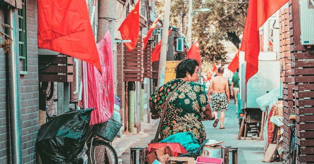 Rua urbana com bandeiras vermelhas suspensas e uma pessoa de bicicleta ao centro.