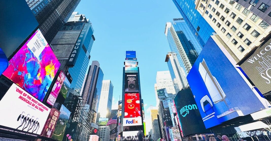 Multidão em Times Square, Nova Iorque, rodeada por arranha-céus e ecrãs gigantes de publicidade, numa imagem típica da vida urbana americana.