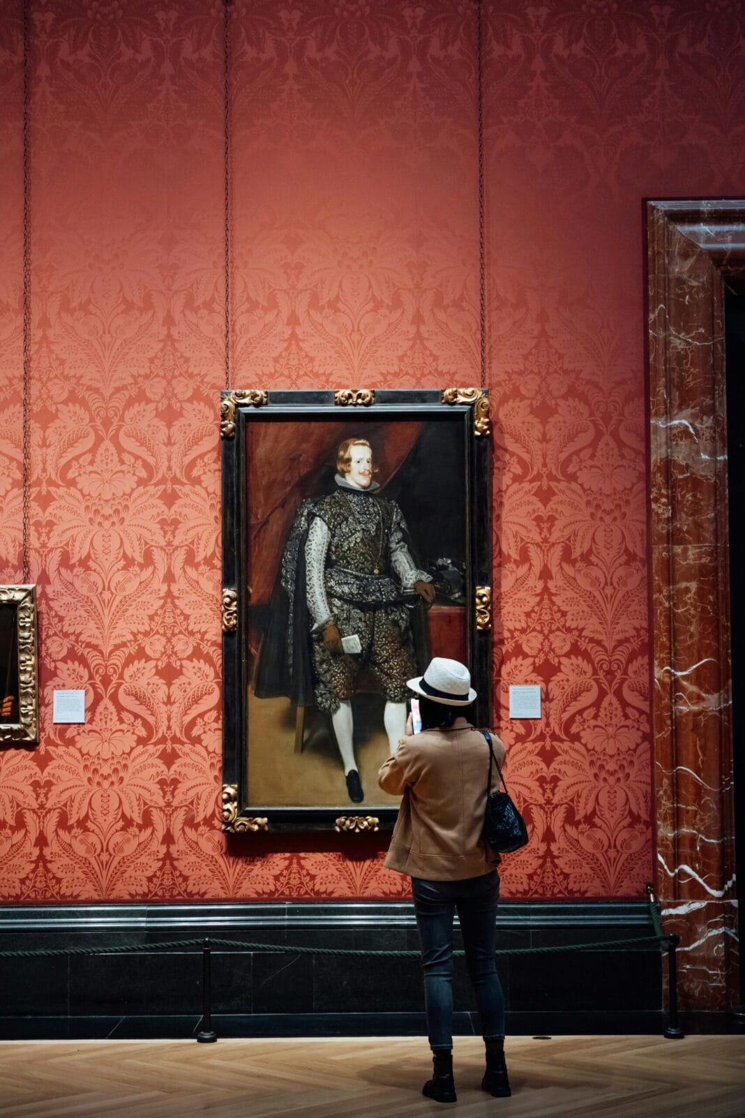 Um visitante observa um retrato histórico numa sala de museu com decoração ornamentada.