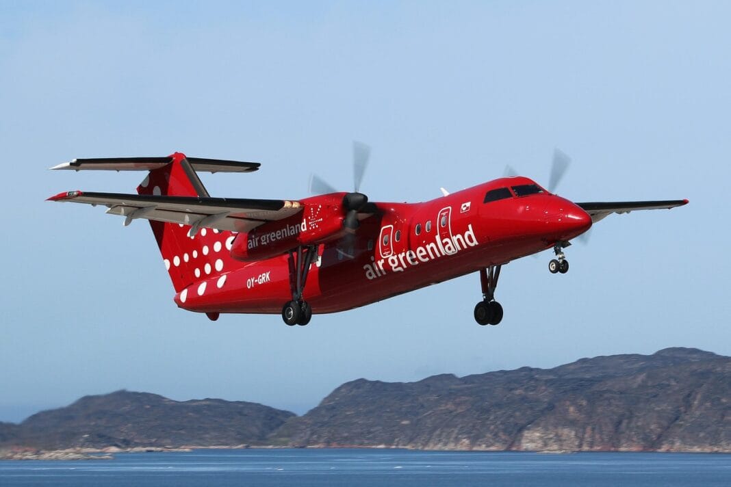 Avião vermelho da Air Greenland a sobrevoar a costa rochosa da Gronelândia.