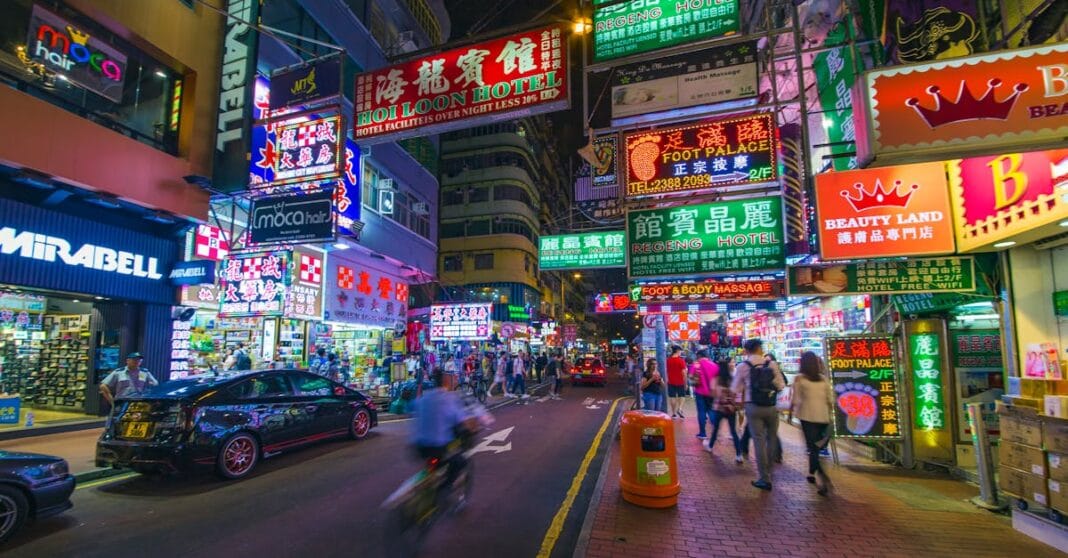 Arranha-céus de Hong Kong ao entardecer, com luzes acesas e céu nublado, sugerindo tensão entre prosperidade e incerteza política.