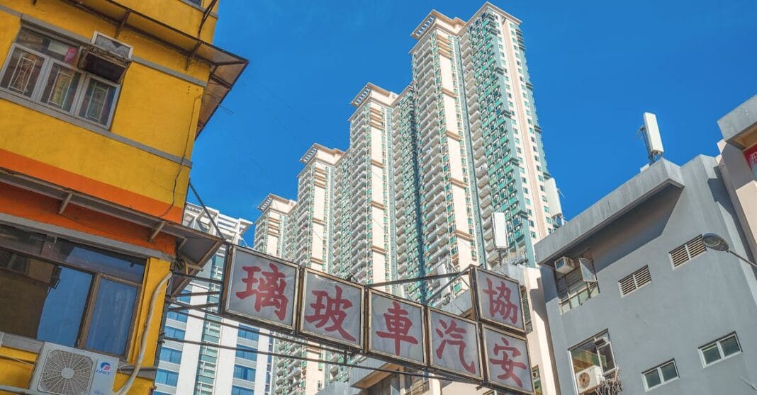 Fachadas com letreiros em chinês e prédios altos modernos ao fundo, vistos de baixo, em Hong Kong.