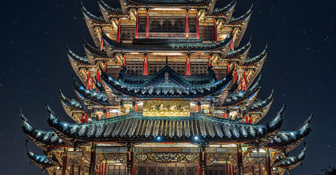 Pagode chinês iluminado à noite, visto de baixo, com telhados sobrepostos e decoração tradicional.