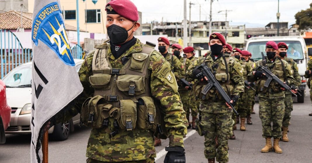 Militares chineses armados marcham em formação durante cerimónia oficial, com bandeira ao fundo.