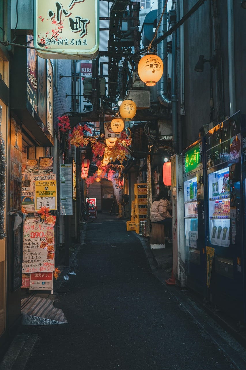 Rua urbana no Japão à noite, com lojas iluminadas e sinais comerciais.