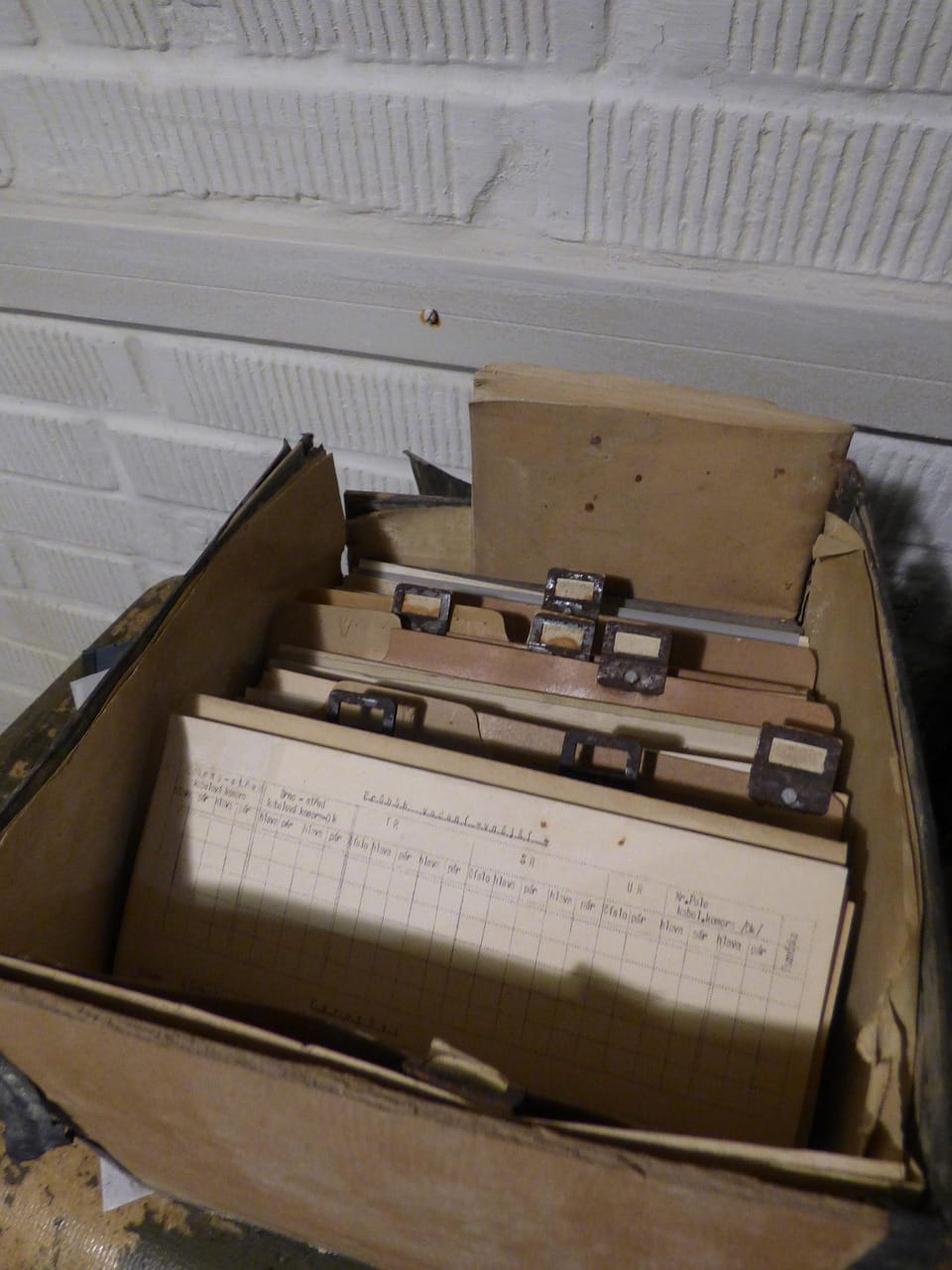 Caixa com dossiers e documentos arquivados, parcialmente visíveis, representando informação fragmentada e organizada em camadas.