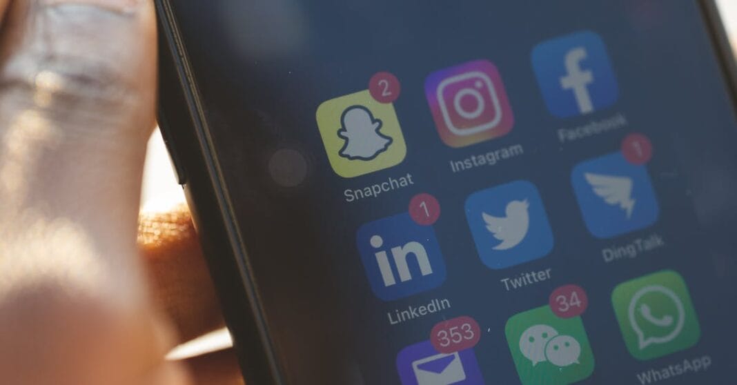 Ecrã de smartphone com ícones de redes sociais e mensagens, alguns com notificações em vermelho.