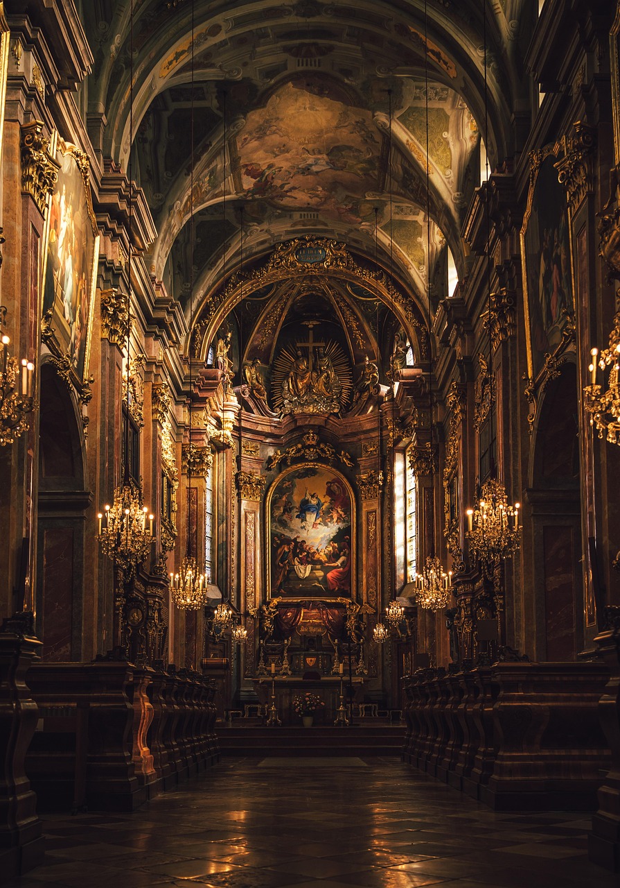 Interior de uma igreja ou catedral, visto de frente, com nave estreita, luz dourada, colunas laterais e altar iluminado ao fundo.