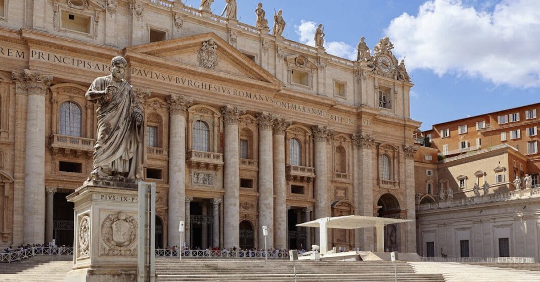 Vaticano Fachada da Basílica de São Pedro, no Vaticano, com a estátua de um apóstolo em primeiro plano e a praça deserta ao fundo.