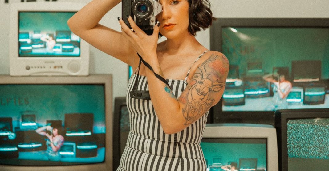Mulher com câmara rodeada por ecrãs de televisão