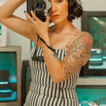 Mulher com câmara rodeada por ecrãs de televisão
