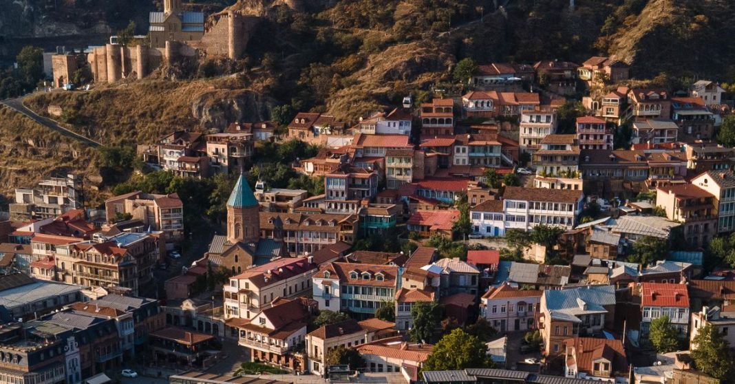 Vista elevada de uma cidade em encosta no Cáucaso do Sul, com casas, edifícios históricos e uma fortificação.