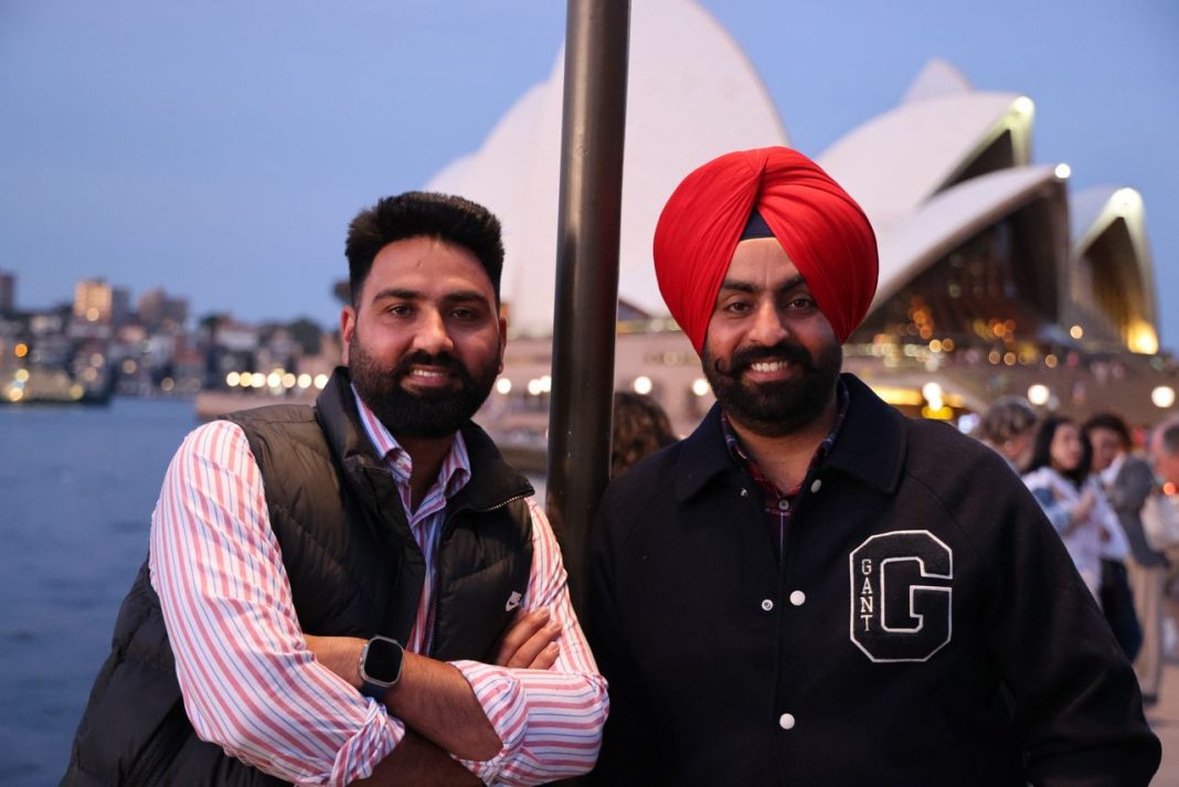 Dois homens junto à Ópera de Sydney, um deles com um turbante vermelho