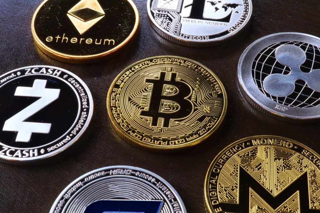 Moedas físicas com símbolos de várias criptomoedas, incluindo Bitcoin, Ethereum e Monero, vistas em detalhe sobre fundo escuro.
