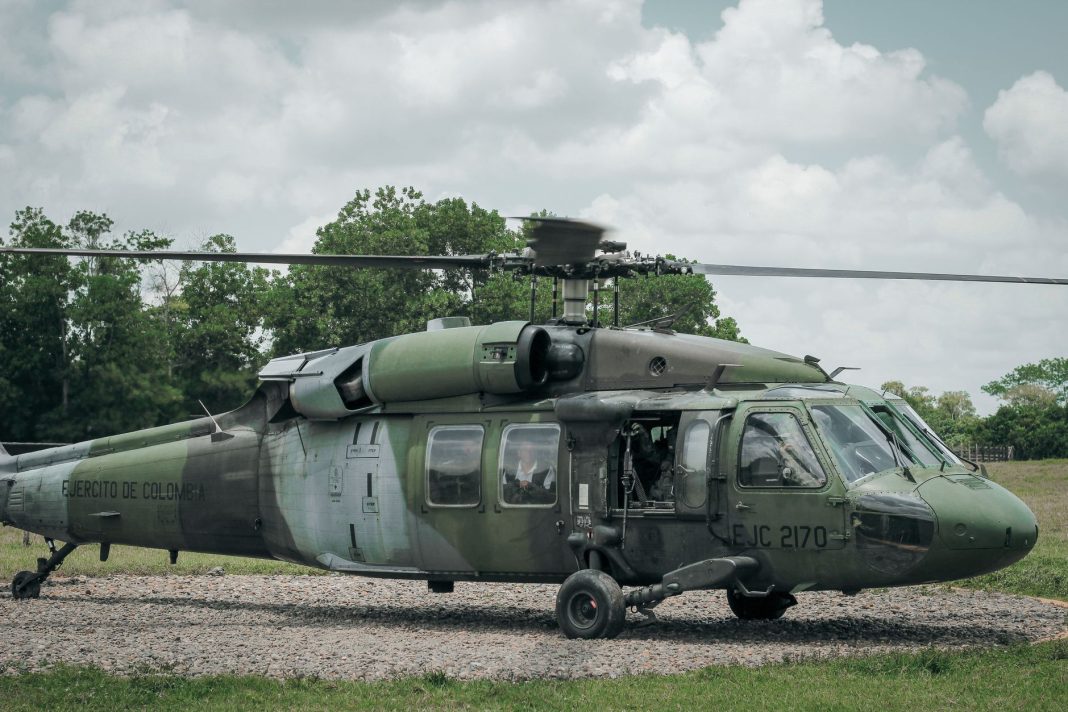 Helicóptero militar verde estacionado em zona aberta, com hélice em movimento, usado para ilustrar prontidão operacional e reforço de defesa.