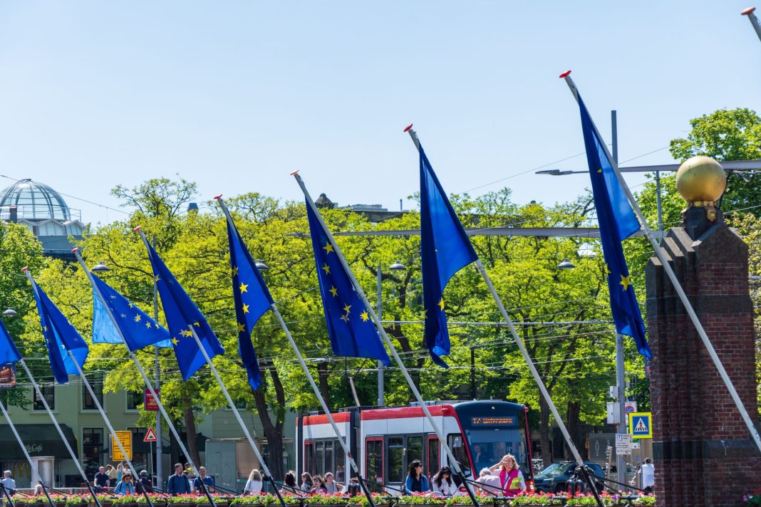 Bandeiras da União Europeia hasteadas em frente ao Parlamento Europeu, em Bruxelas, simbolizando a política europeia de defesa e a autonomia estratégica.