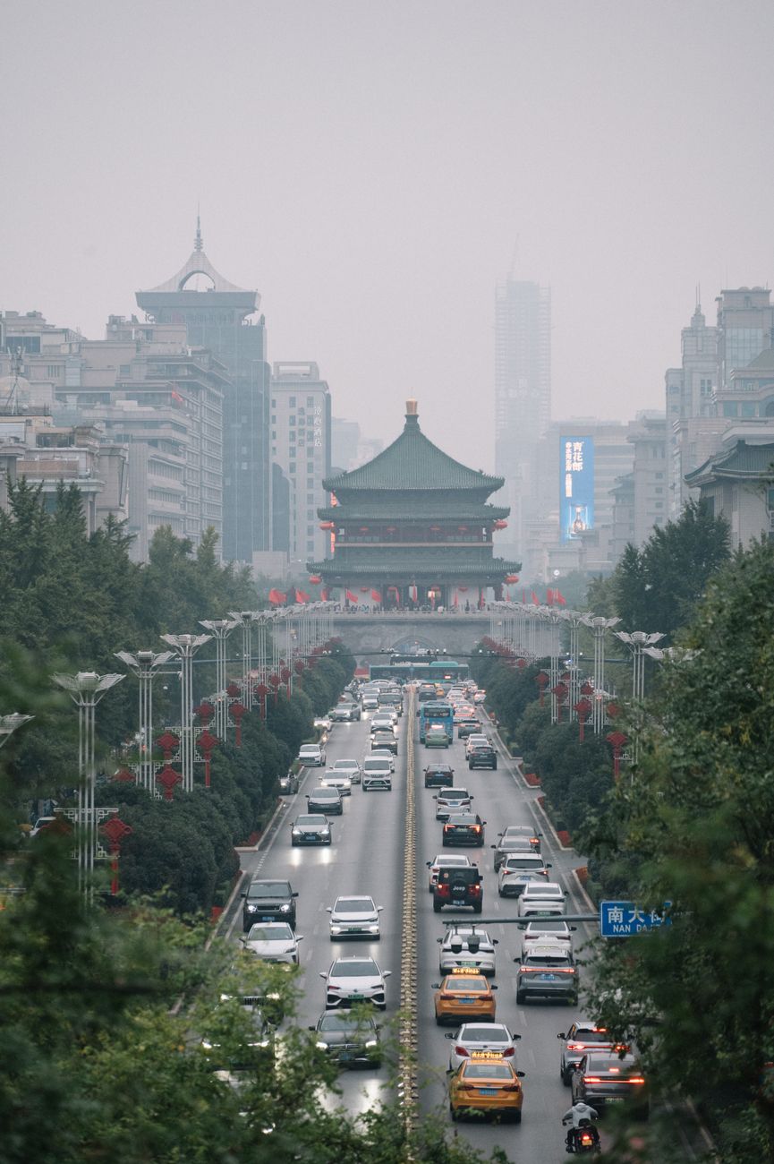 Pavilhão tradicional chinês, de colunas vermelhas e telhado em telha verde-azulada com beirais recurvos, em primeiro plano, com arranha-céus de vidro do distrito financeiro de Pequim ao fundo, sob céu limpo.