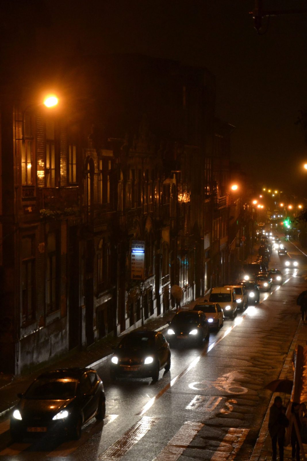 Rua do Porto à noite, com automóveis, luzes urbanas e pavimento molhado.