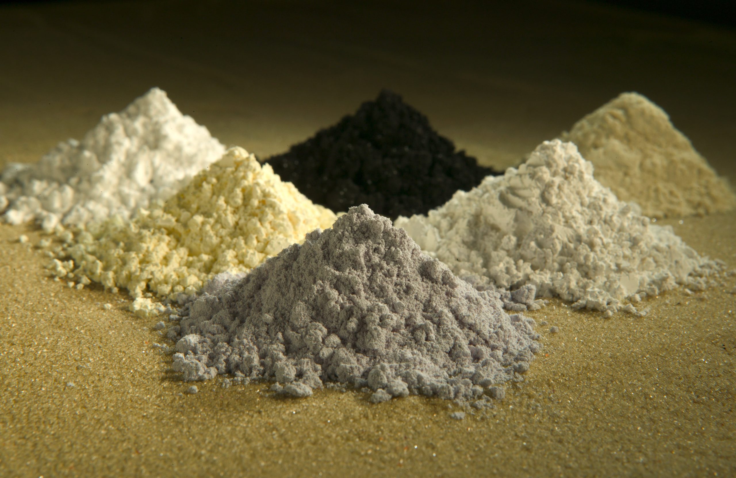 Amostras de óxidos de terras raras de diferentes cores sobre uma superfície preta.