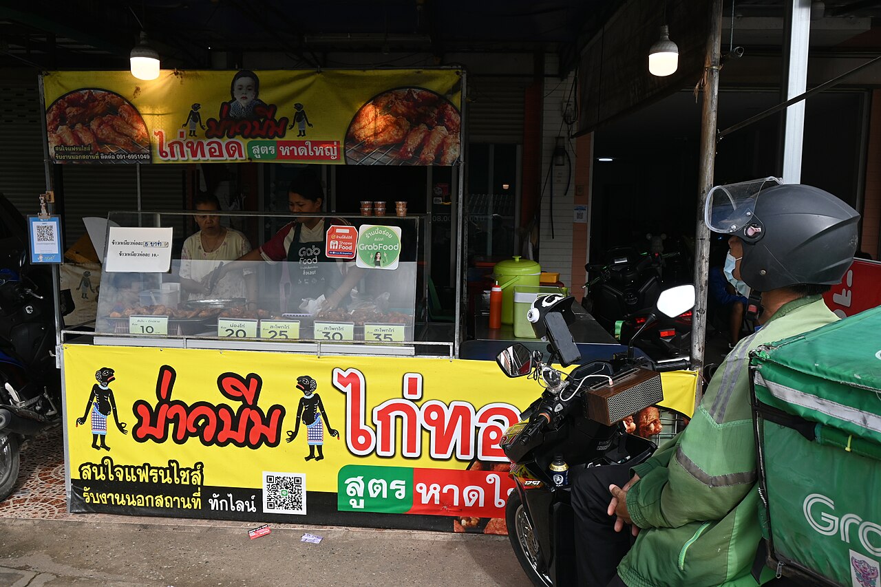 Estafeta GrabFood junto de uma banca de comida na Tailândia