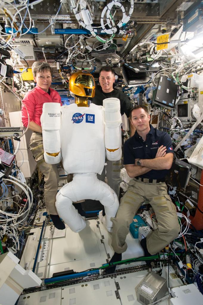 Três astronautas junto do Robonaut, imagem ilustrativa da interação humana com robôs humanoides em Portugal.