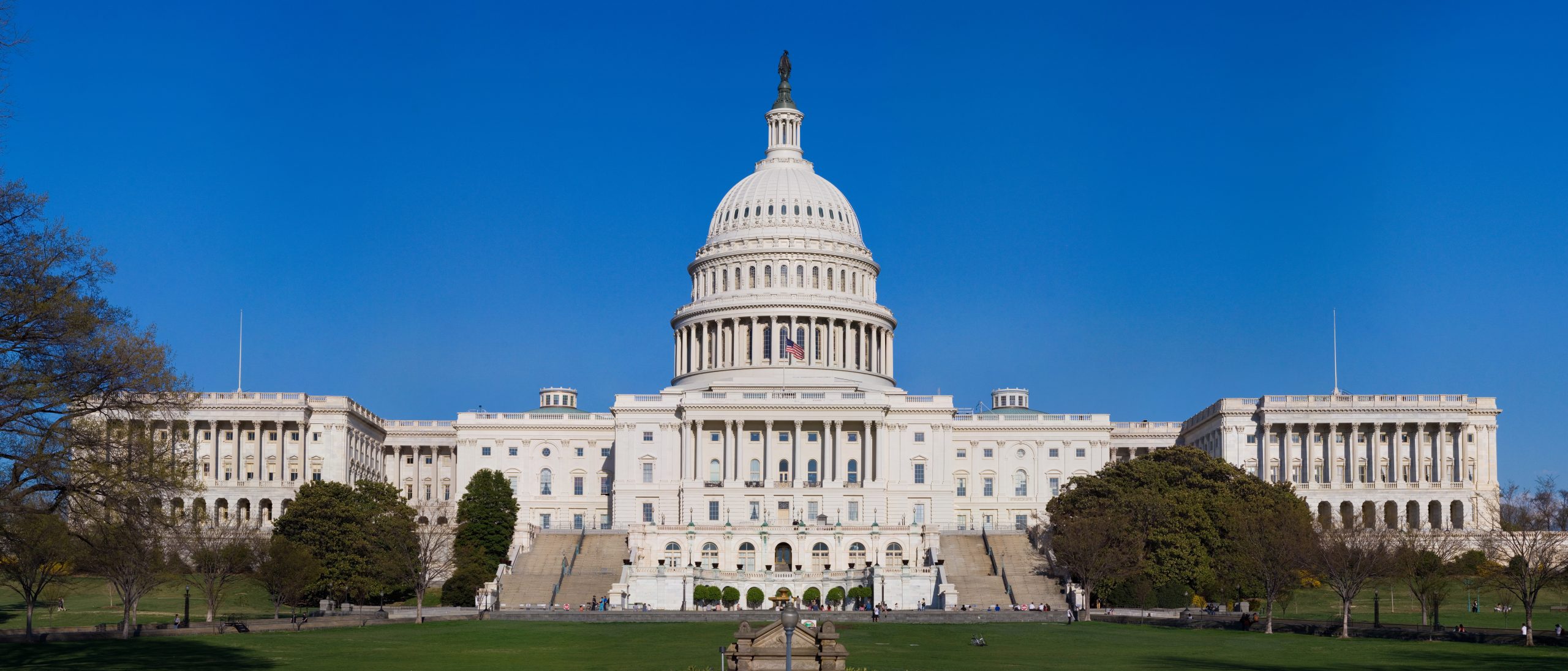 Fachada oeste do Capitólio dos Estados Unidos, com a cúpula ao centro e relvado em primeiro plano.